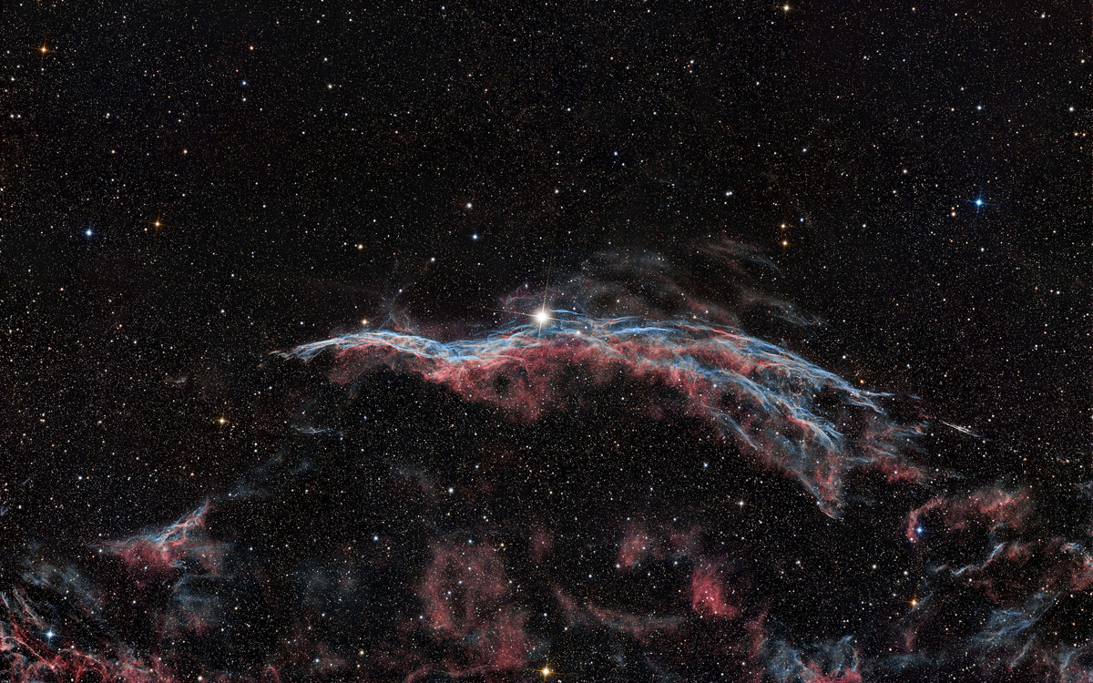 A star-filled deep space scene with a glowing nebula in red, pink, and blue tones against a black background.